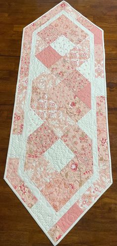 a pink and white quilted table runner on a wooden floor with wood floors in the background