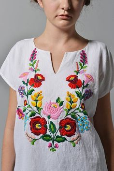 a woman wearing a white shirt with colorful flowers on it's chest and shoulders