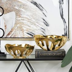 two golden bowls sitting on top of a black shelf next to a book and plant