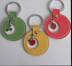 three different colored leather keychains with an apple and strawberry on them