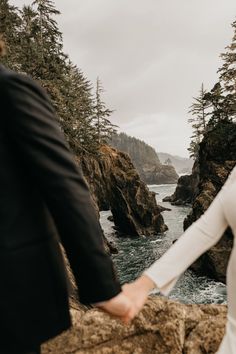 a bride and groom hold hands as they stand on rocks near the ocean