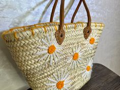 a straw bag with daisies on it sitting on a wooden table next to a white wall