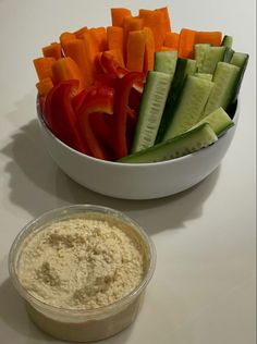 a white bowl filled with cucumbers and carrots next to a container of dip