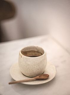 a white cup and saucer sitting on top of a table next to a wooden spoon