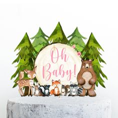 a cake topper with woodland animals and the words oh baby on it, surrounded by pine trees