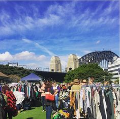 people are shopping at an outdoor flea market with sydney bridge in the background, australia