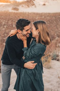 a man and woman embracing each other on the beach in front of some sand dunes