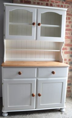 a white china cabinet with two doors and drawers on the top, in front of a brick wall