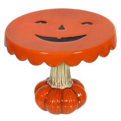 an orange pumpkin shaped cake stand with a jack - o - lantern face on it