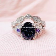 an image of a ring that is on top of a pink blanket with diamonds and blue stones