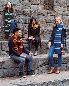 four people sitting on stone steps in front of a rock wall and one person standing