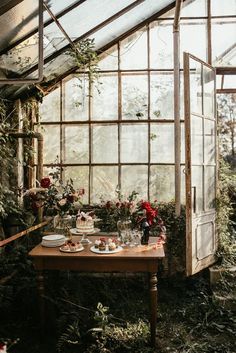 a wooden table topped with plates and cups next to a window filled with greenery