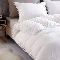 a bed with white comforters and pillows on it next to a night stand in a bedroom