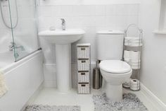 a white toilet sitting next to a sink and bath tub in a bathroom with gray rugs on the floor