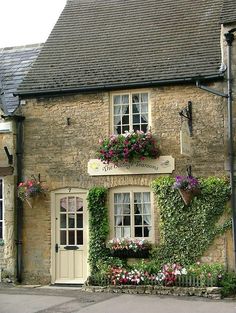 an old brick building with flowers growing on it's side and windows above the door