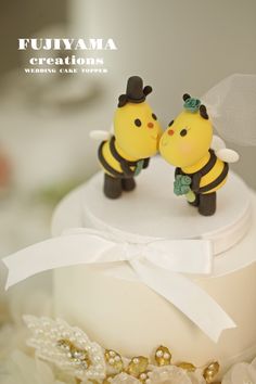 two small yellow and black bee figurines on top of a white wedding cake