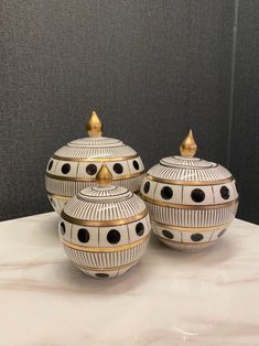 three white and gold decorated jars on a table with black dots around the top one