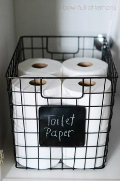 two rolls of toilet paper in a wire basket with a chalkboard sign on it