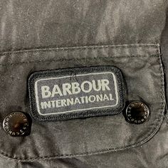 Belted Waxed Bike Jacket, by Barbour International, in a blue waxed cotton. The jacket has a belt around the waist and four large pockets on the front. It features a Union Jack lining and has a small Union Jack on the back of the collar. The branding is in grey rather than the usual yellow, with Barbour press studs and zips throughout. In good condition, the spoke of neck fastening is missing. Measurements Bust: 38" Length: 26" Sleeves : 24" Winter Cotton Outerwear With Logo Patch, Cotton Outerwear With Logo Patch For Work, Outdoor Cotton Outerwear With Logo Patch, Cotton Outerwear With Logo Patch For Outdoor, Cotton Biker Outerwear With Pockets, Bike Jacket, Jack Flag, Union Jack Flag, Barbour International