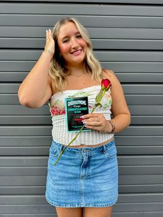 a woman wearing a white top and blue denim skirt holding a rose in her hand