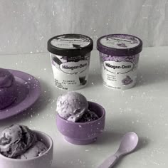 three ice creams in purple bowls on a white surface with two spoons next to them