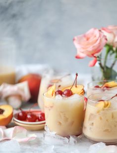 two glasses filled with ice and cherries on top of a table next to peaches