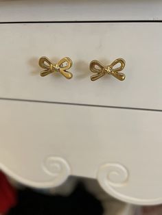 two gold bow shaped earrings sitting on top of a white dresser