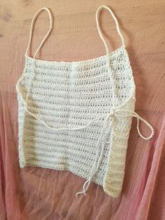 a white crochet top hanging up on a pink bed sheet with two ties