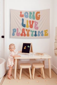 a baby sitting at a table in front of a wall with a sign on it that says long live playtime