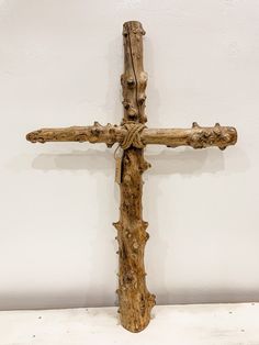 a large wooden cross with vines on the bottom and sides, in front of a white wall