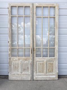 an old pair of double doors sitting in front of a garage door with glass panes