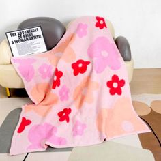 a pink flowered blanket sitting on top of a white chair next to a book