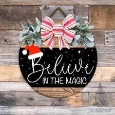 a sign that says believe in the magic with a santa hat on it and greenery