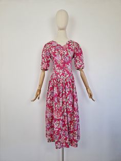 Vintage 90s Laura Ashley cottagecore floral cotton dress. Featuring scalloped neckline, fitted bodice and a skirt gathered under the waistline with a pocket. Fastens with fabric cover buttons at the bodice and a zip at the side. Made from flowy cotton fabric. Floral print in the shades of green, pink, purple mauve, red and white on the bright pink background. Fabric: 100% cotton Brand: Laura Ashley Very good vintage condition The modern size is recommendation only, please refer to measurements. Fitted Vintage Cotton Dress With Floral Print, Cotton Cottagecore Floral Dress For Garden Party, Cottagecore Floral Cotton Dress For Garden Party, Cottagecore Cotton Floral Dress For Garden Party, Cottagecore Prairie Dress With Floral Print For Daywear, Cottagecore Floral Print Dress For Daywear, Fitted Floral Print Prairie Dress For Daywear, Cottagecore Floral Dress For Daywear, Cotton Floral Print Prairie Dress With Short Sleeves