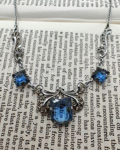 Gorgeous vintage Art Deco necklace with open back blue glass set in chrome filigree. The blue glass is a vibrant sapphire colour and the setting reminds me of a butterfly, which I think is uniquely lovely. There is also a mark on the clasp ring but I can't make it out. In very good vintage condition with some wear to the chrome finish (please see photos), and could use a thorough clean by someone who knows what they're doing. The necklace is 41cm long and the centre stone measures 1.1cm by 0.9cm Blue Victorian Filigree Jewelry, Antique Blue Necklaces For Formal Occasions, Antique Blue Filigree Necklace, Victorian Blue Filigree Necklace, Antique Blue Necklace With Intricate Design, Ornate Blue Pendant Necklace, Victorian Blue Necklaces For Formal Occasions, Blue Victorian Necklace For Formal Occasions, Victorian Style Blue Necklaces For Formal Occasions