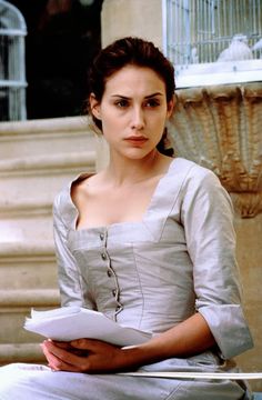 a woman sitting on the ground with a book in her hand and looking at the camera