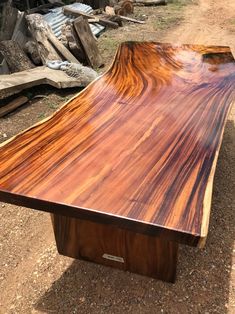 a large wooden table sitting on top of a dirt road next to a pile of wood