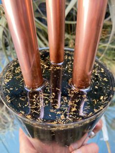 three copper colored candles are in a glass holder with black and gold flakes on it