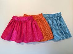 three different colored skirts hanging up against a white wall, one is blue and the other is pink