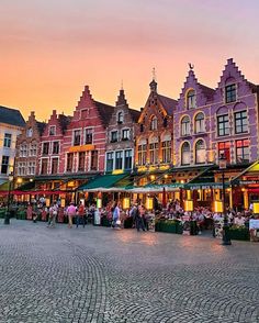 many people are sitting at tables in front of some colorful buildings on the cobblestone street