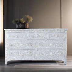 a white dresser sitting on top of a hard wood floor next to a potted plant