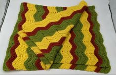 a crocheted dishcloth is laying on a white surface with a green, yellow and red striped design