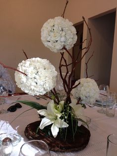 white flowers are arranged in a vase on a dining room table with wine glasses and silverware