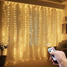 a person is holding a remote control in front of a curtain with lights on it