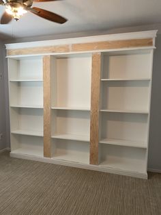 an empty room with white bookcases and a ceiling fan