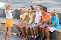 several children are sitting on the curb and pointing at something in the air with their hands up