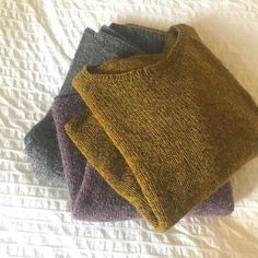 three sweaters sitting on top of a bed next to each other in different colors