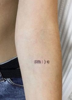 a woman's arm with the word smile tattooed on her left arm, in black ink