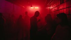 a group of people standing in a dark room with red light coming from the ceiling