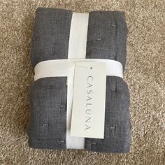 a gray and white blanket with a tag on it sitting on the floor next to a carpet